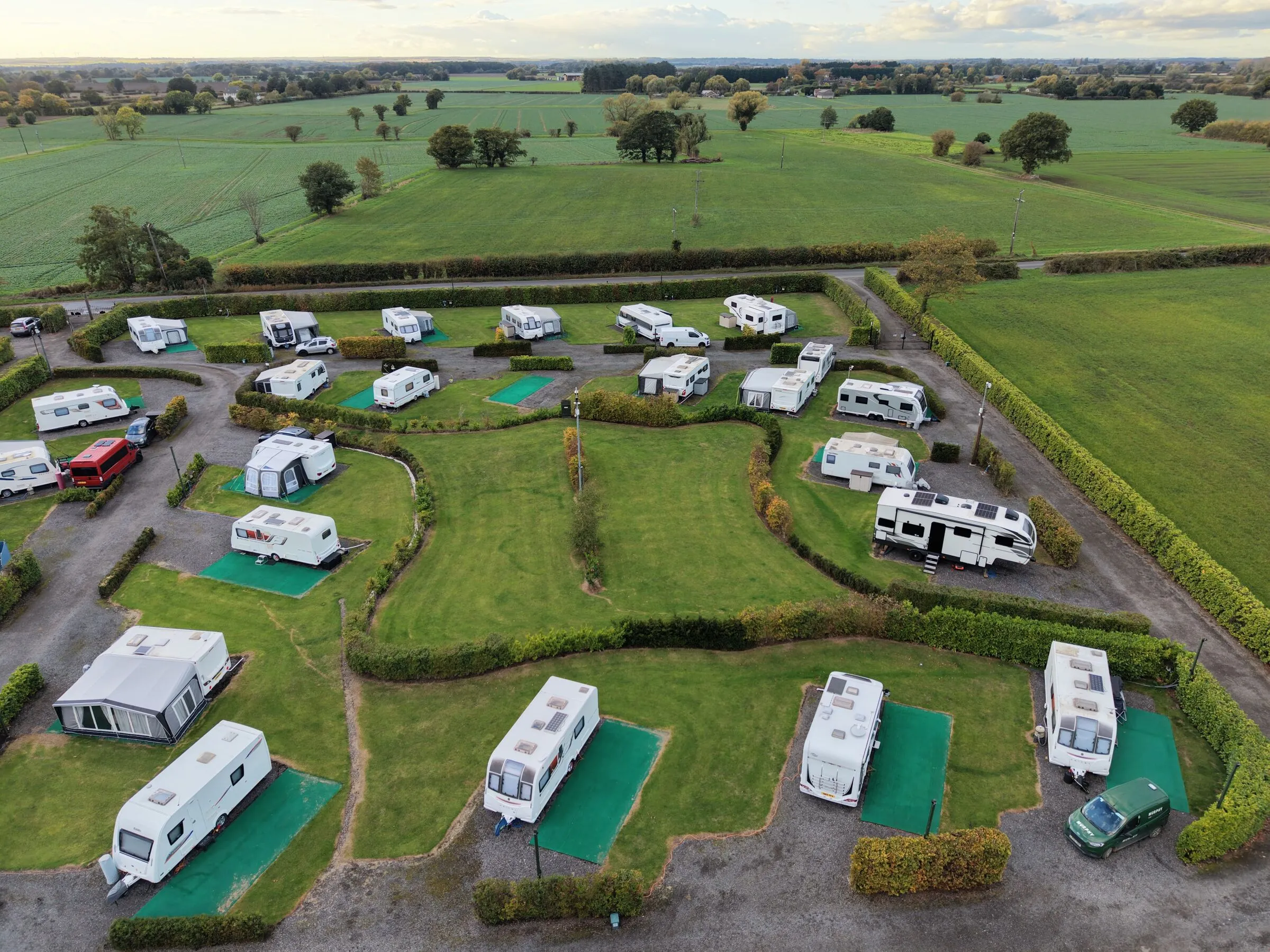 Aerial view of caravans on hedged hard-standing pitches with green awning bases around a central lawn
